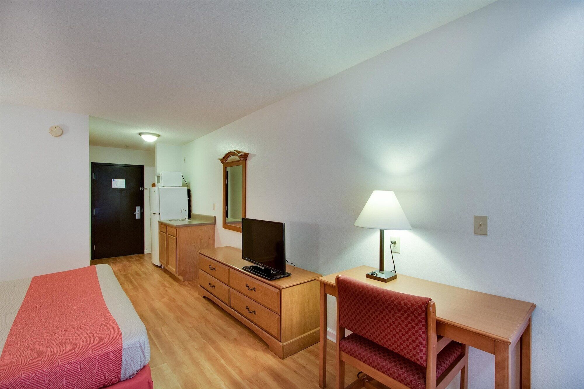 A hotel room with a bed, a desk with a chair, a dresser, a television, and a lamp.