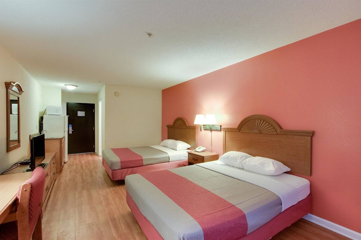 A hotel room with two beds, a desk, a chair, and a TV.