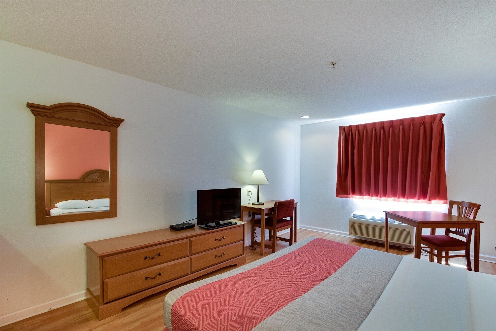 Una habitación de hotel con cama, televisión, escritorio con silla, cómoda y ventana con cortinas.