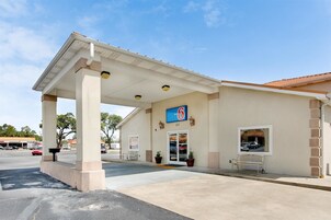 A motel with a covered parking area, a sign indicating it's number 6, and a visible entrance with a bench outside.