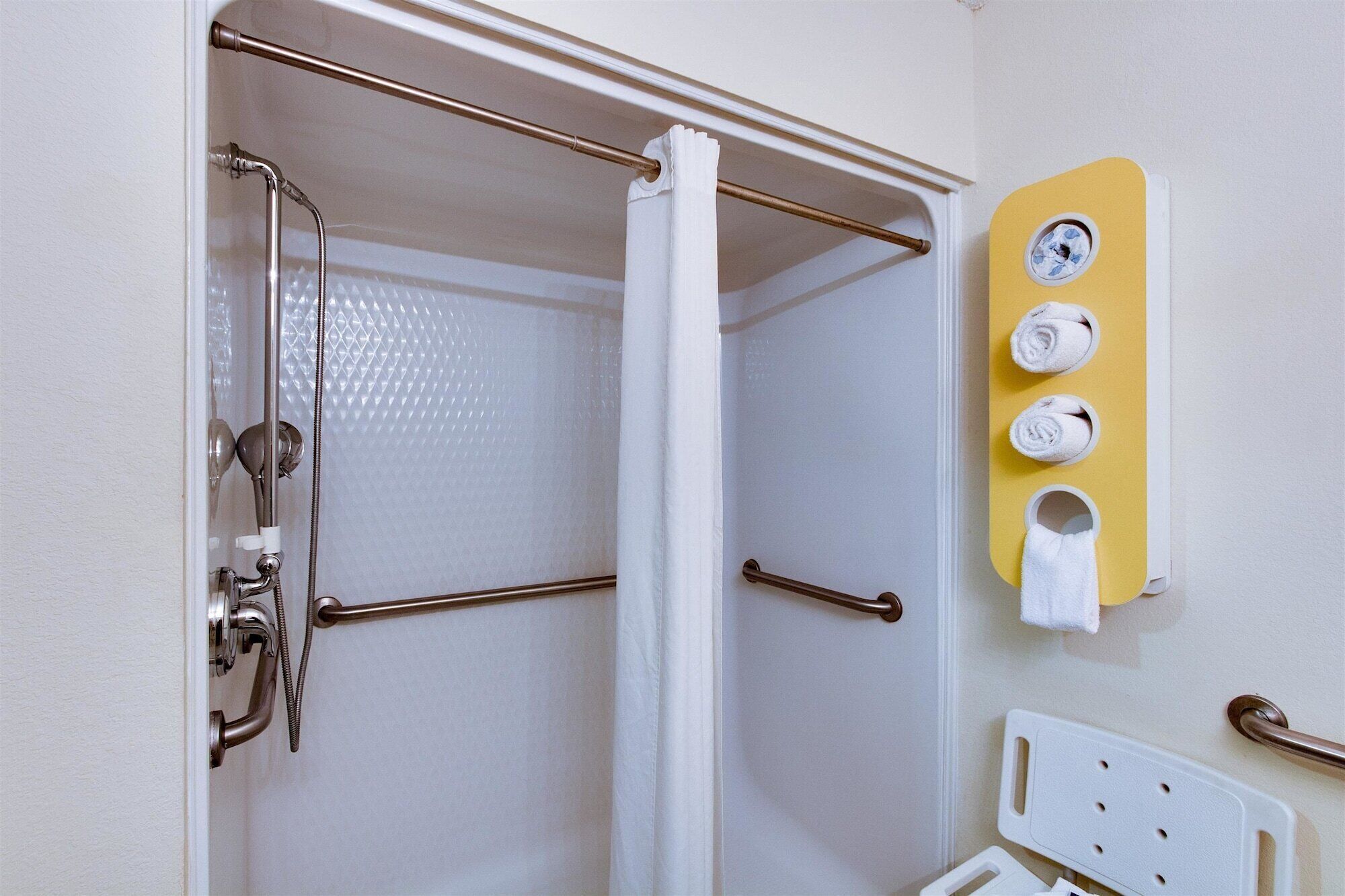A bathroom with a shower, grab bars, and a towel rack with towels.