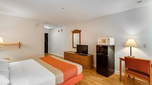 Een hotelkamer met een bed, een bureau, een koelkast, een televisie en een spiegel.
