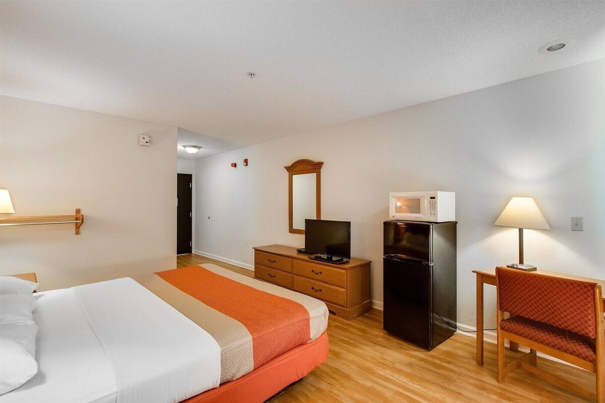 A hotel room with a bed, a desk, a refrigerator, a television, and a mirror.