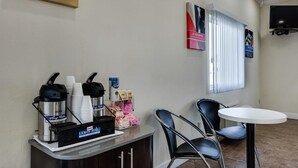 Een koffiehoek met een koffiezetapparaat, bekers en een koffieautomaat. Er staat een tafel en een stoel in de ruimte.