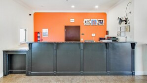 Een receptiegedeelte met een donker receptiebalie, een oranje wand en een deur. Er hangen ingelijste foto's en certificaten aan de muur.