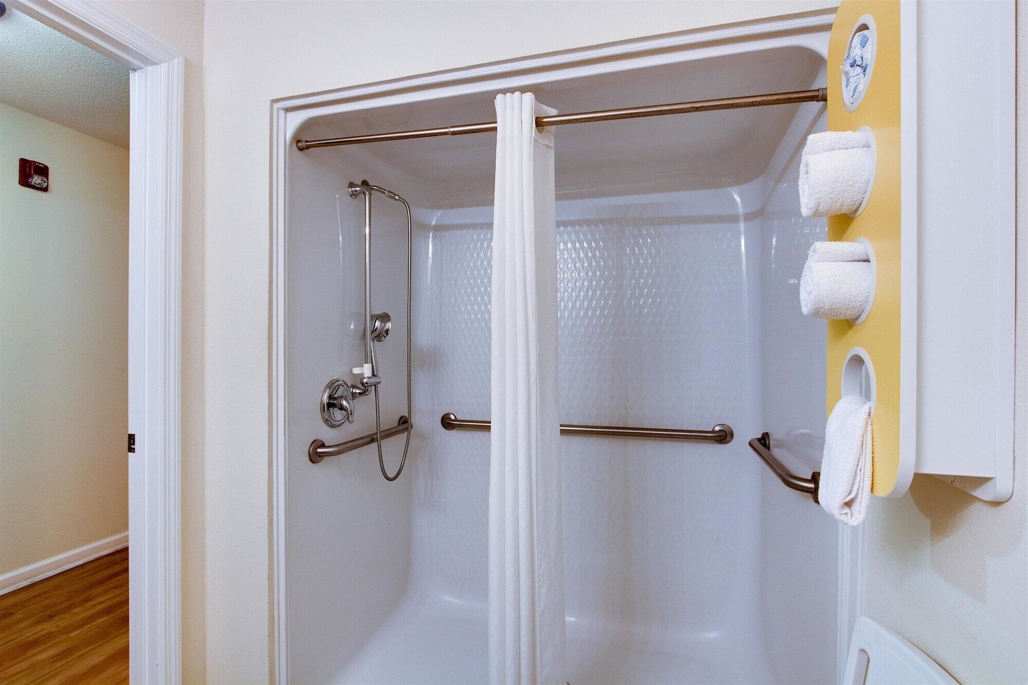 A walk-in shower with a glass door, grab bars, and a towel rack with towels.