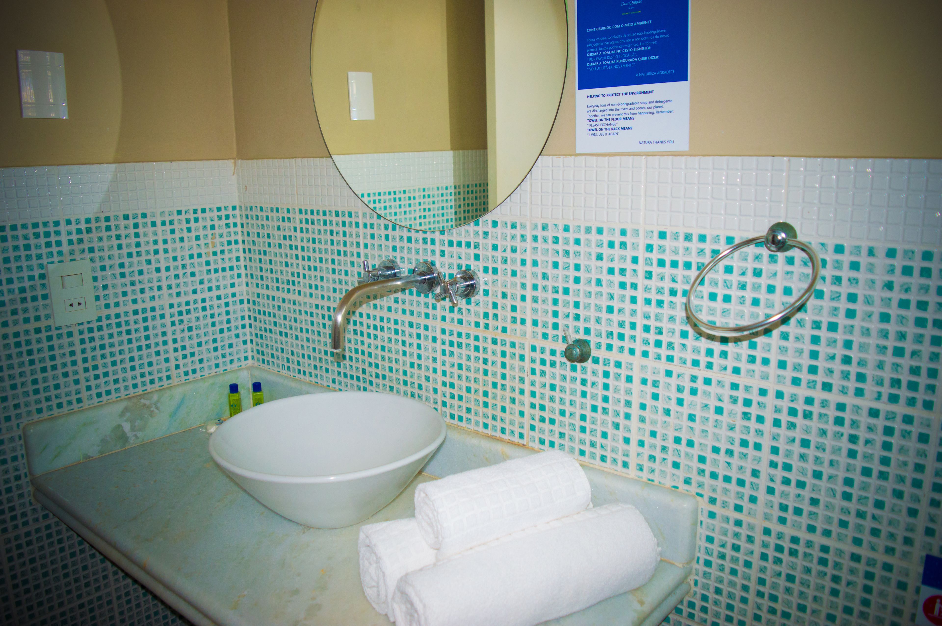 Un baño con un lavamanos blanco, un espejo y un perchero para toallas.