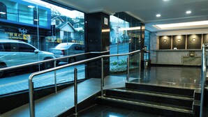 A hotel lobby with a reception desk, a staircase with metal railings, and a view of the street outside. - Hotel San Rafael Comfort Class (Foz do Iguaçu)