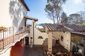 A courtyard with a stone floor, a white building with a balcony, and a tiled roof. - Hotel Tenuta Il Burchio (Figline e Incisa Valdarno)