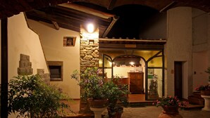 Un patio exterior con muros de piedra, plantas en macetas y una puerta de madera que da a un espacio interior.