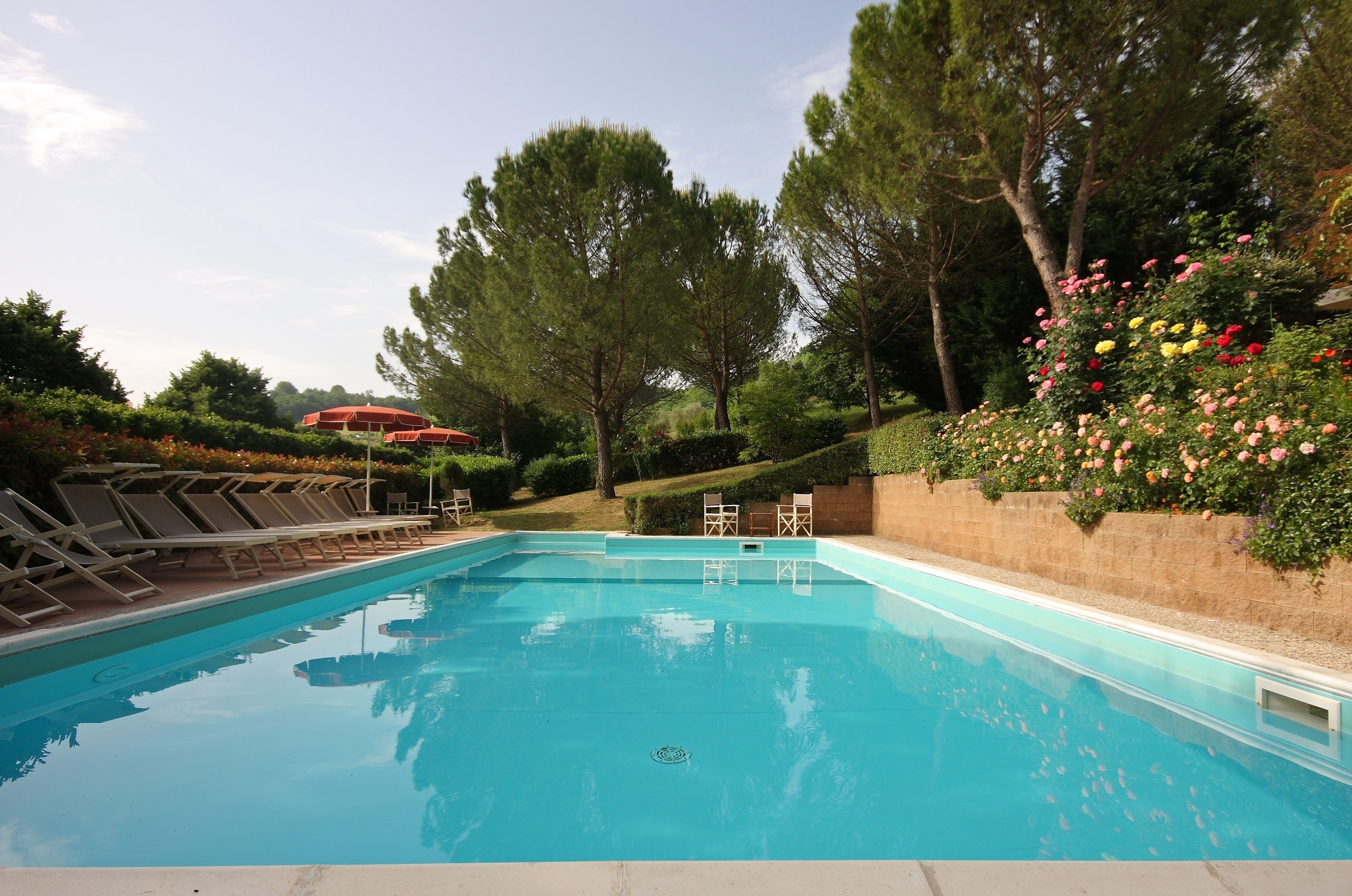 A swimming pool with lounge chairs and a red umbrella in the background.
