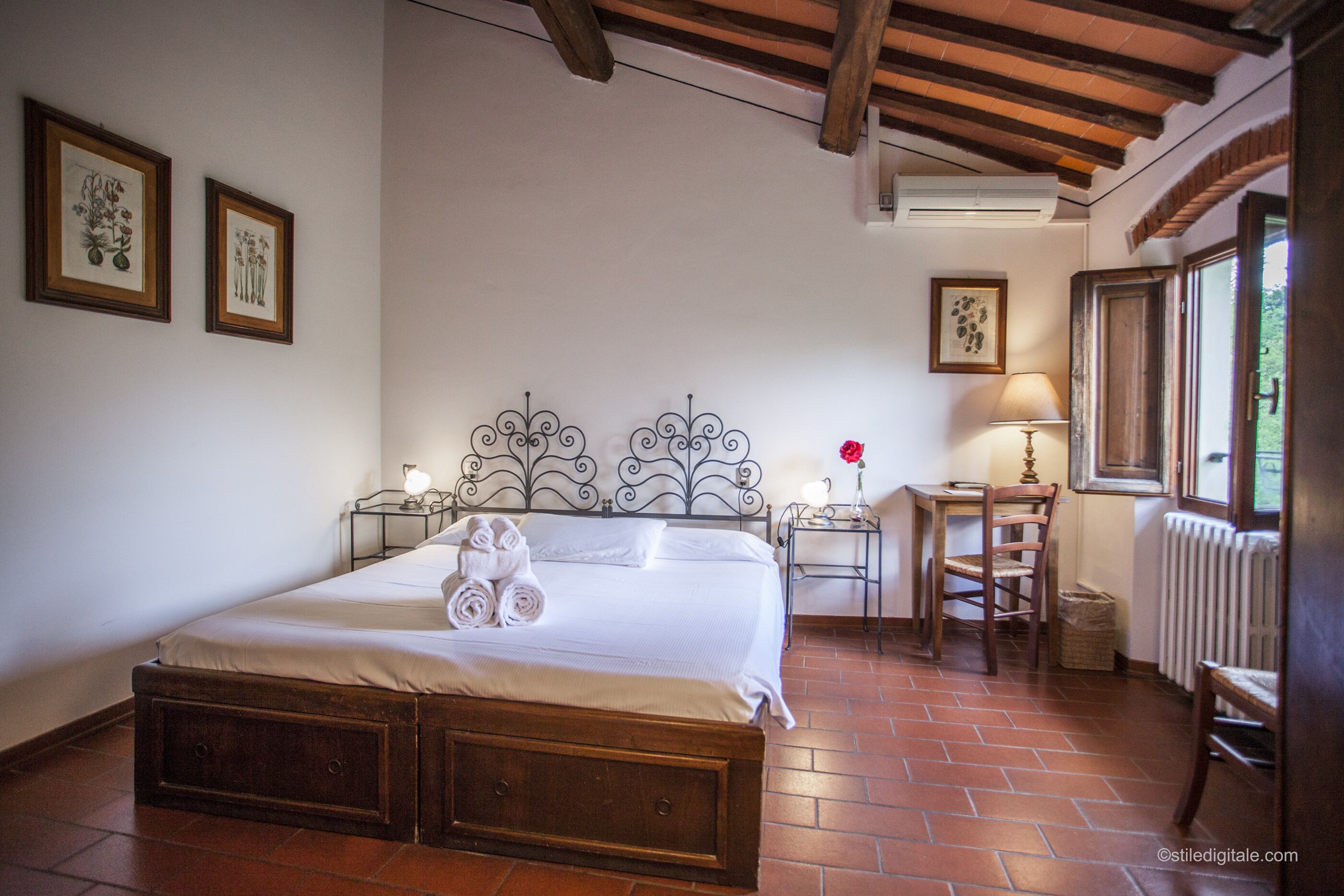 A bedroom with a wooden bed, two bedside tables with lamps, a radiator, and a window with a view.