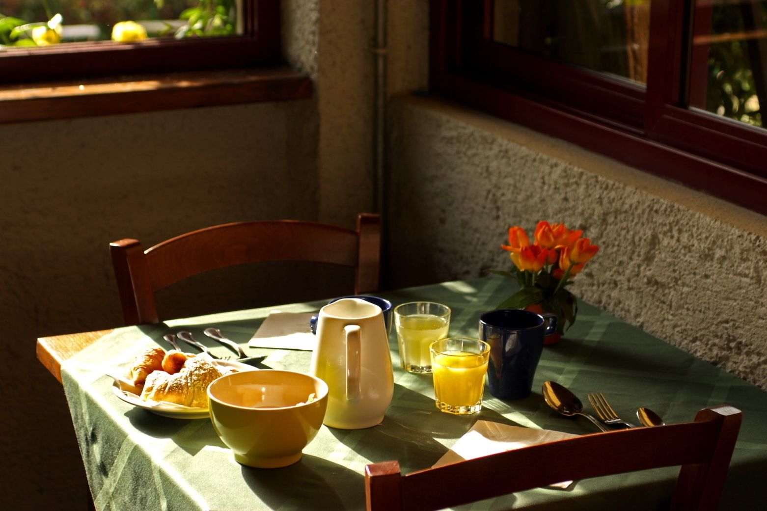 Una mesa de desayuno con una jarrón, tazones, vasos y un florero.