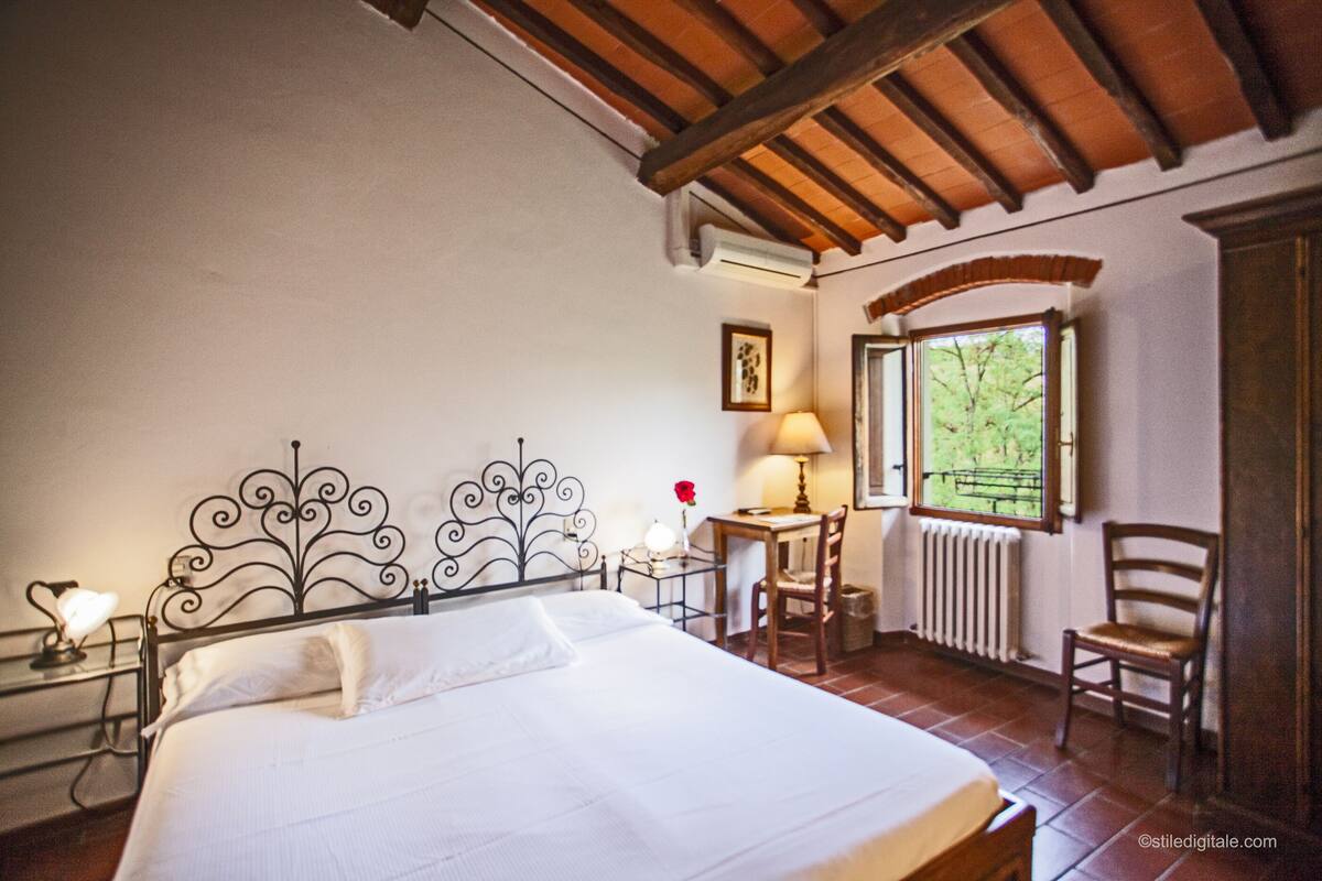 Un dormitorio con cama, escritorio, dos sillas, ventana y radiador.