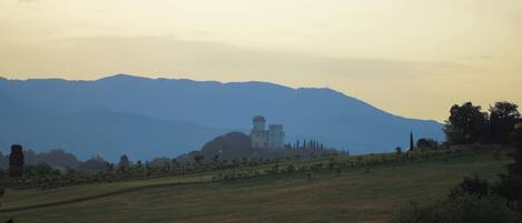 A rural landscape with a prominent building on a hill, surrounded by fields and distant mountains.