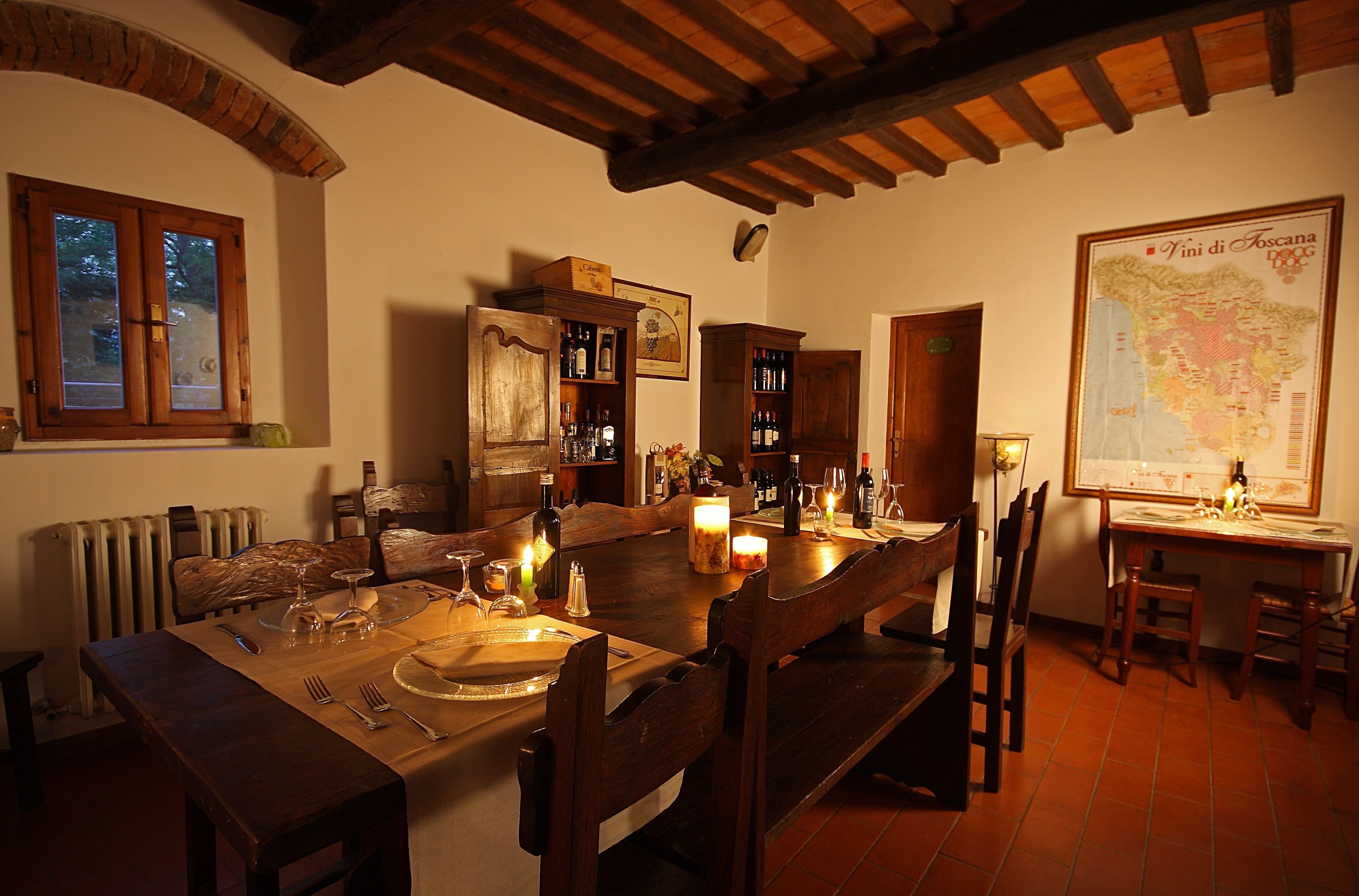 Un comedor con una mesa de madera dispuesta para una comida, rodeada de sillas. Hay botellas de vino y copas sobre la mesa, y un mapa en la pared.