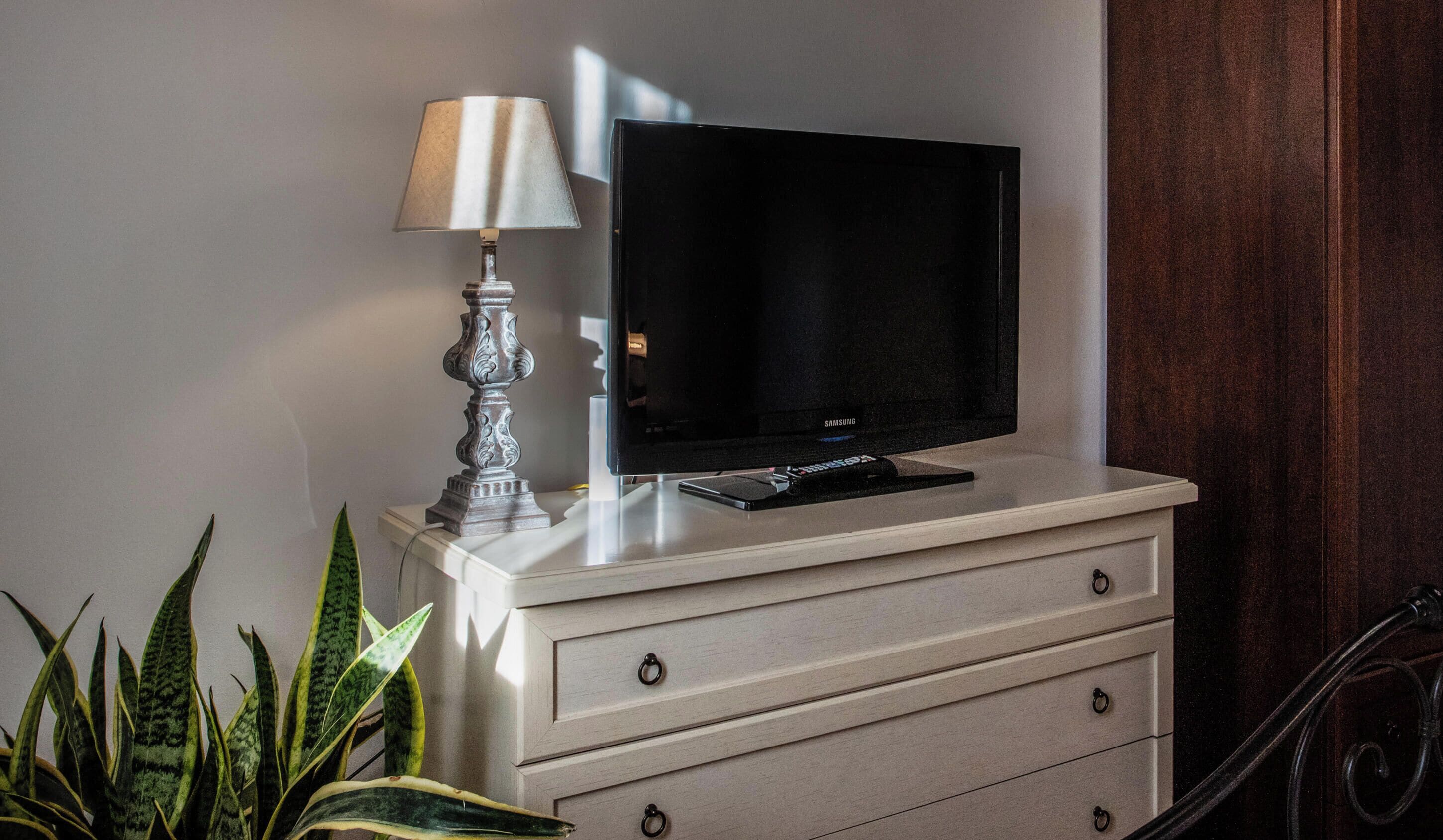 Un televisor sobre un mueble con cajones, una lámpara y una planta.