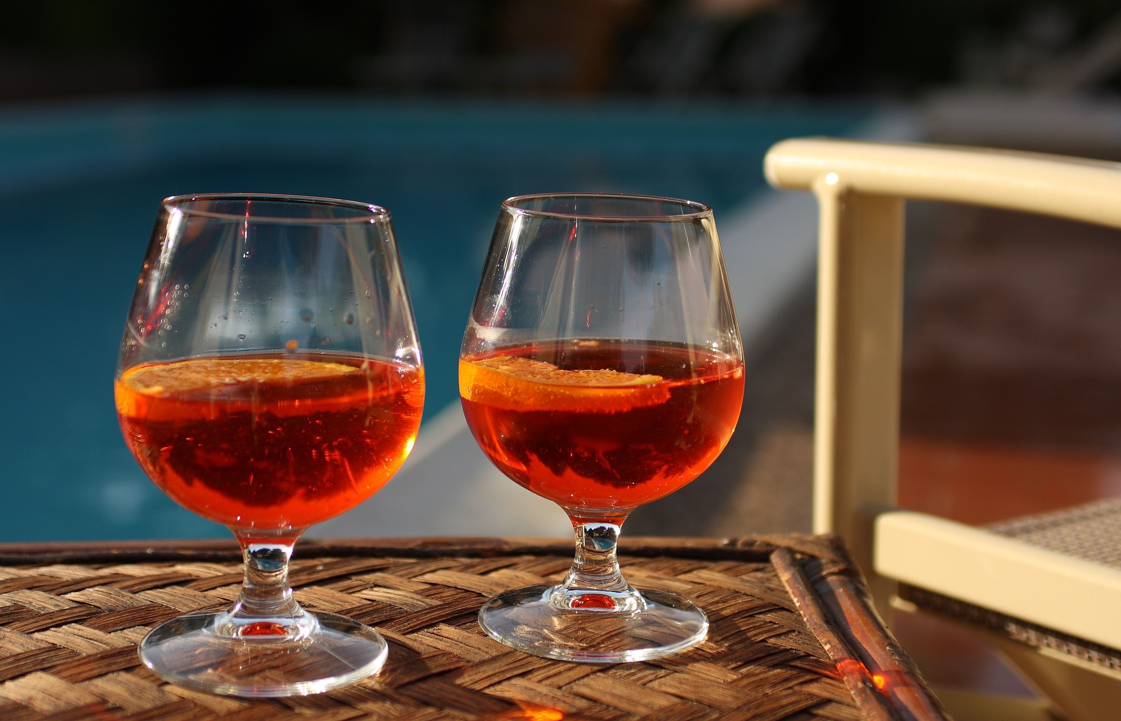 Due bicchieri di bevanda rossa su un tavolo in rattan vicino a una sedia a bordo piscina.