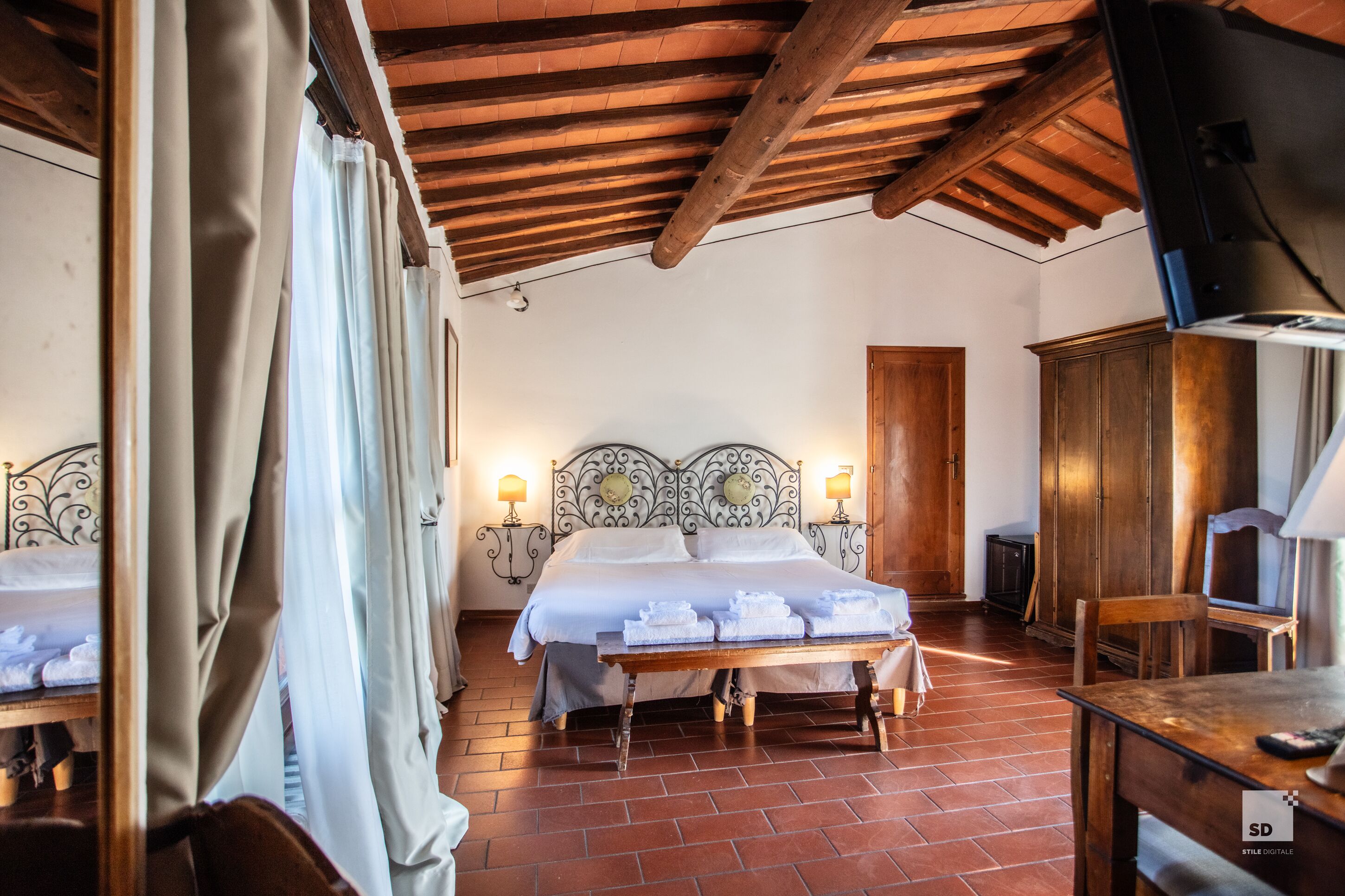 Habitación de hotel con techo de madera, cama doble con ropa de cama blanca, dos lámparas de noche, armario de madera y un televisor sobre un mueble de madera.