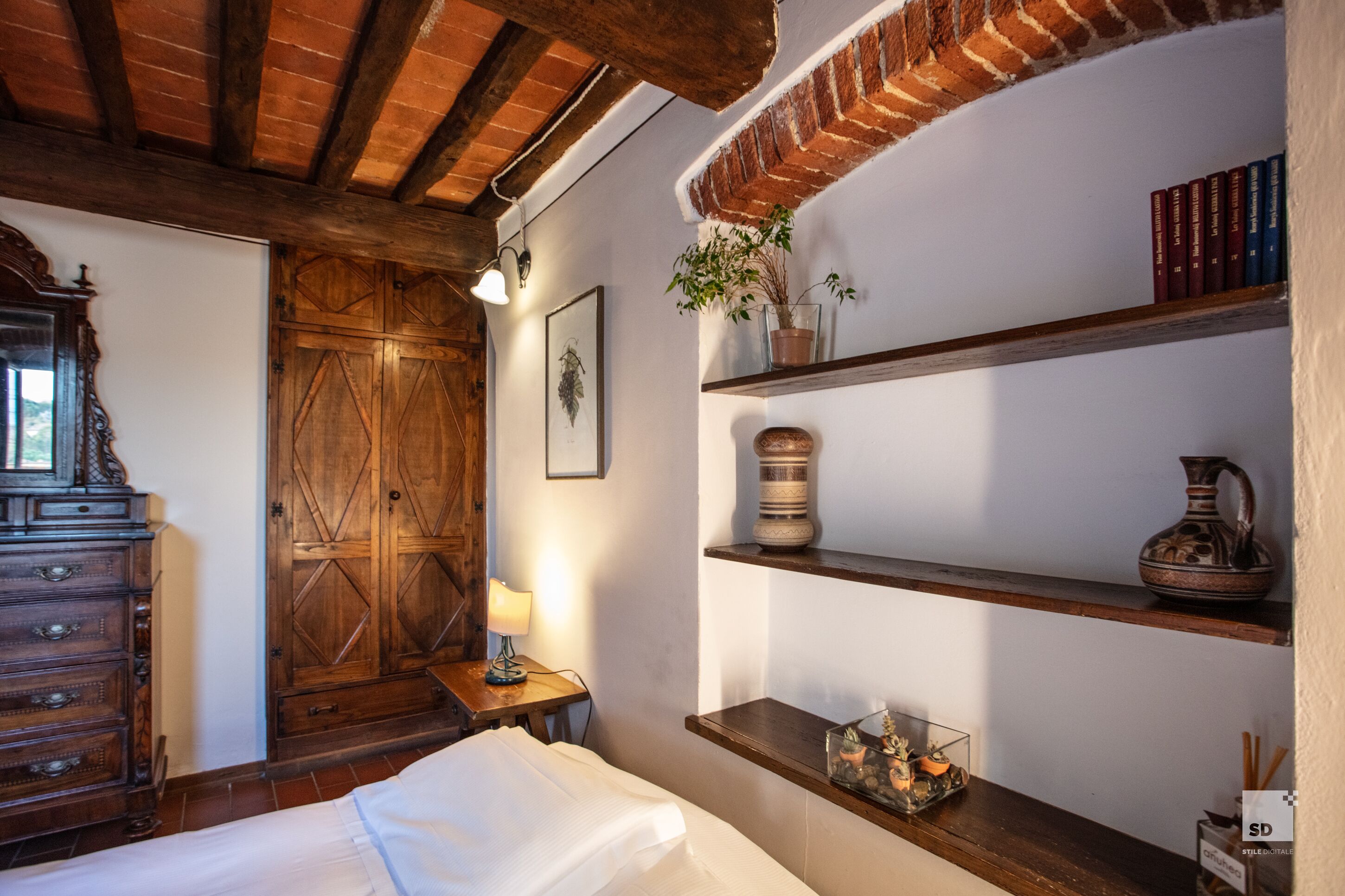 Une pièce chaleureuse avec un lit en bois, une commode, un mur en briques et des étagères remplies de livres et d’objets décoratifs.
