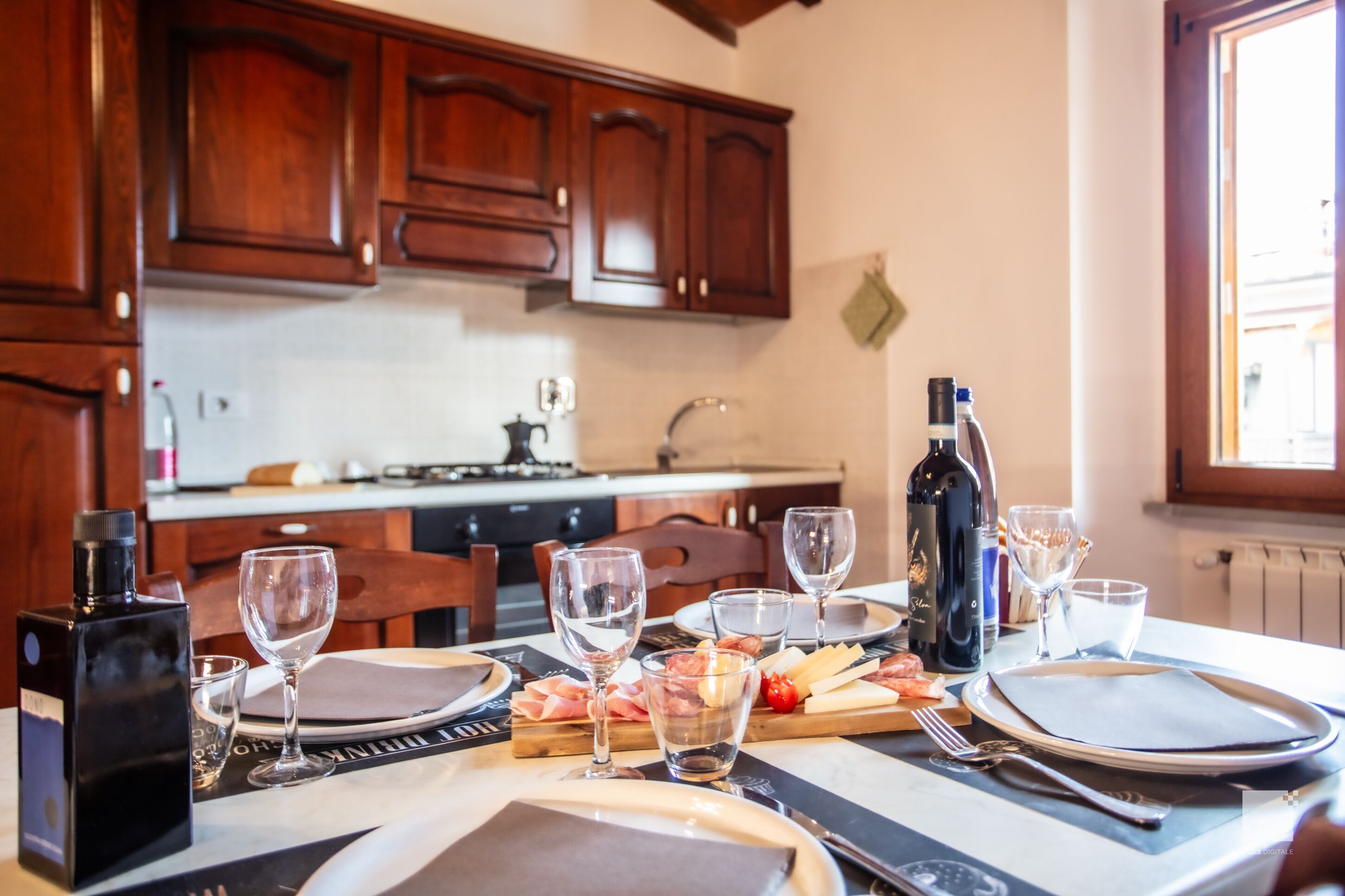 A dining table set with plates, cutlery, glasses, and a bottle of wine.