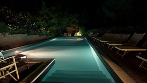 Una piscina con escalones de acceso, rodeada de sillas de descanso y una pared de piedra con vegetación.