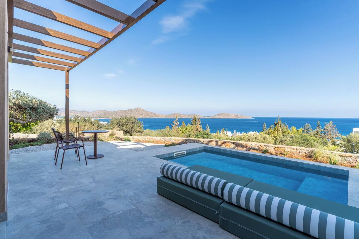 A pool area with a view of the sea, a pergola, and outdoor furniture.