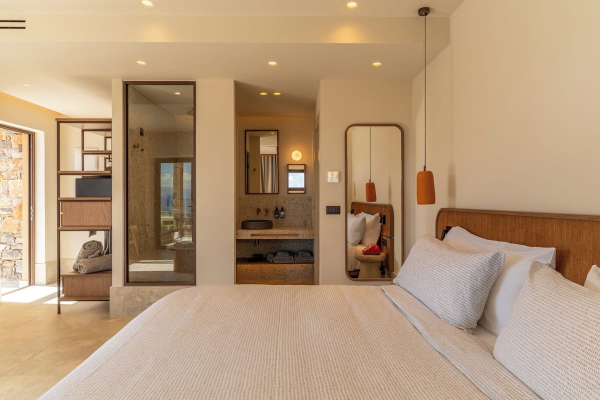 Una habitación de hotel moderna con una cama grande, un baño con espejo y una pared de piedra.