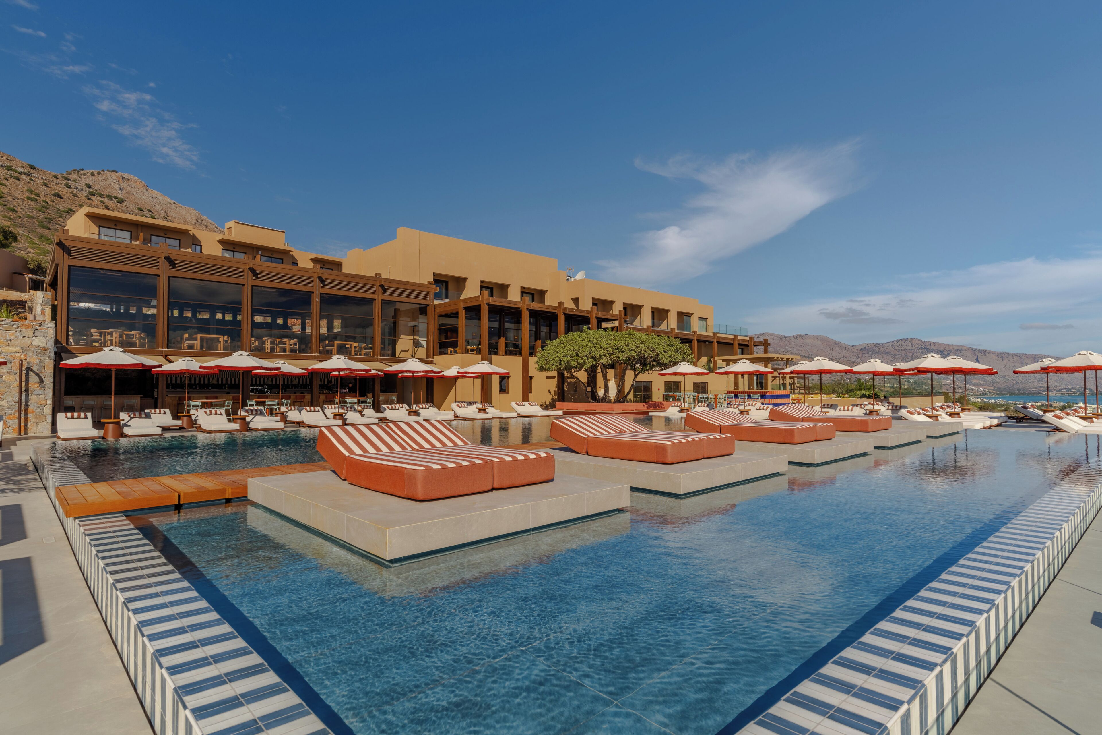 A pool area with lounge chairs and umbrellas, a building with large windows, and a clear sky.