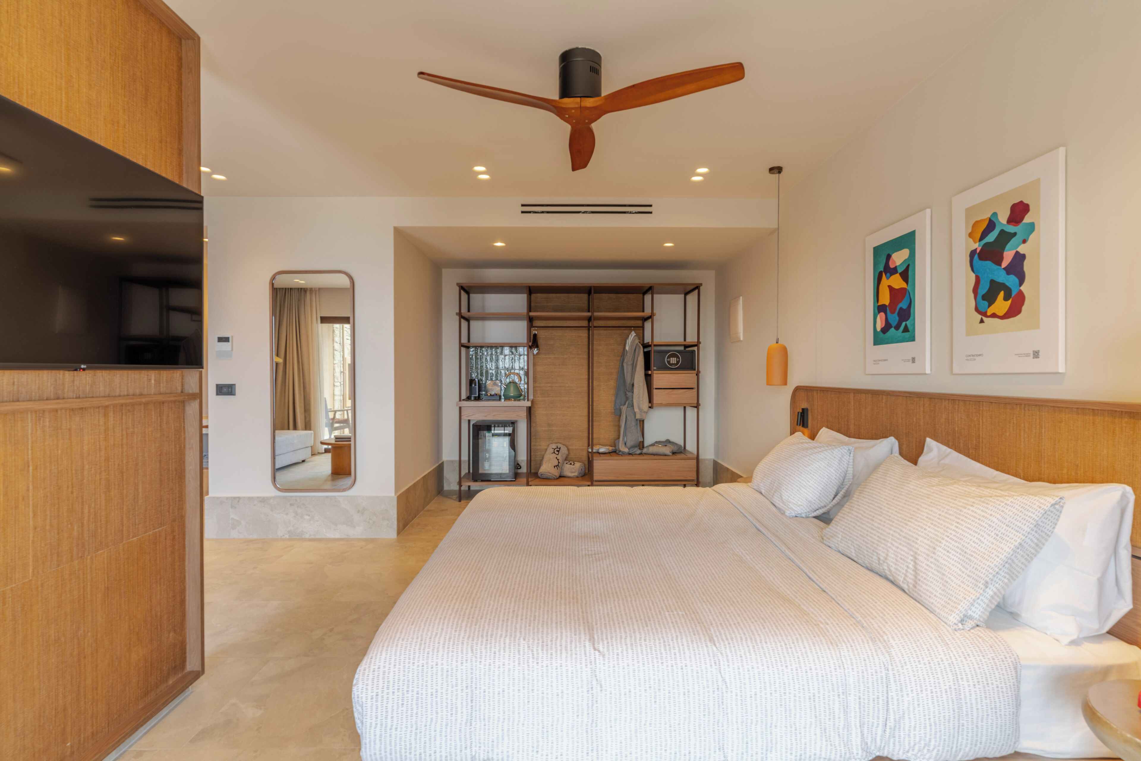 Una habitación de hotel moderna con una cama grande, cabecera de madera, ventilador de techo y obras de arte en las paredes.