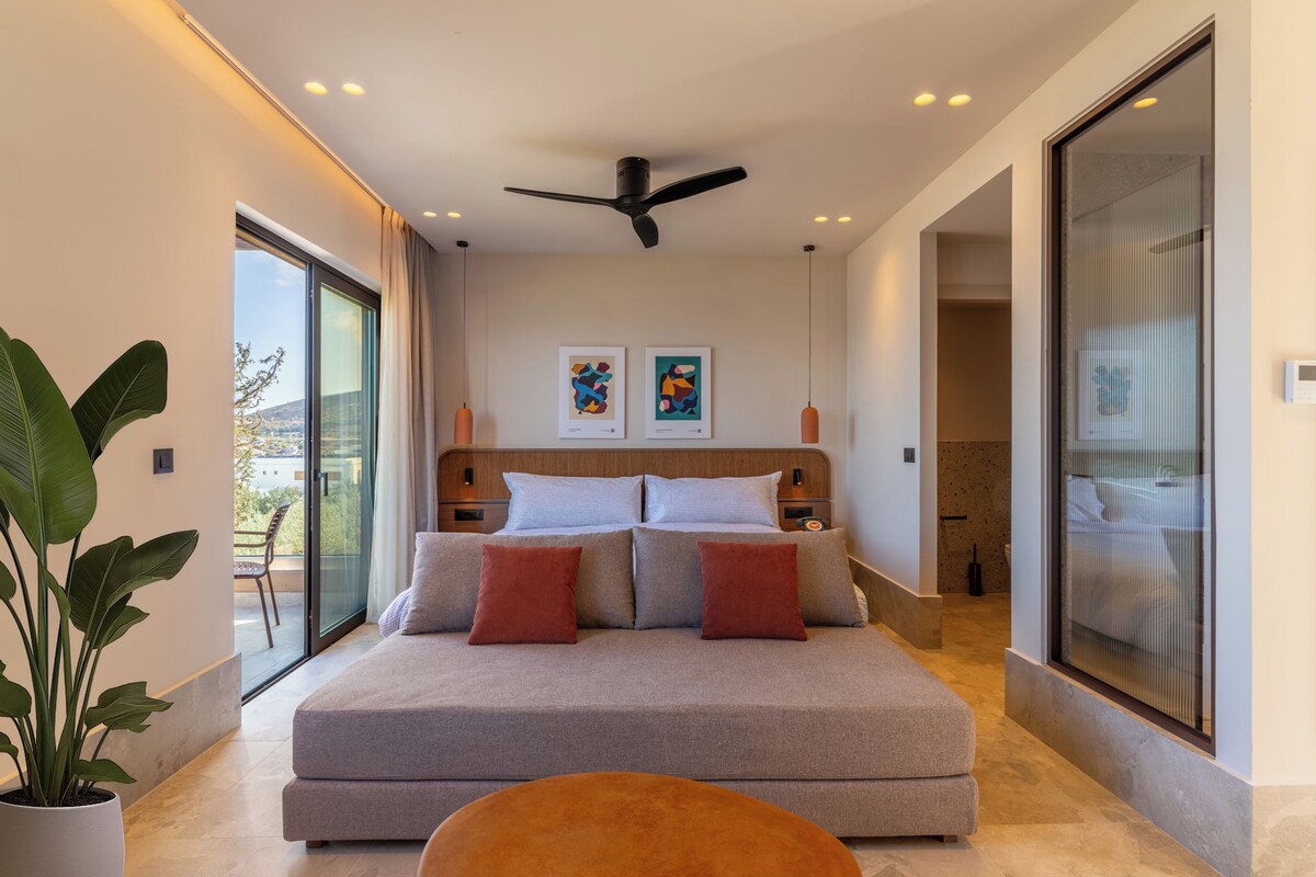 A modern bedroom with a large bed, a ceiling fan, artwork on the wall, and a balcony with a view.