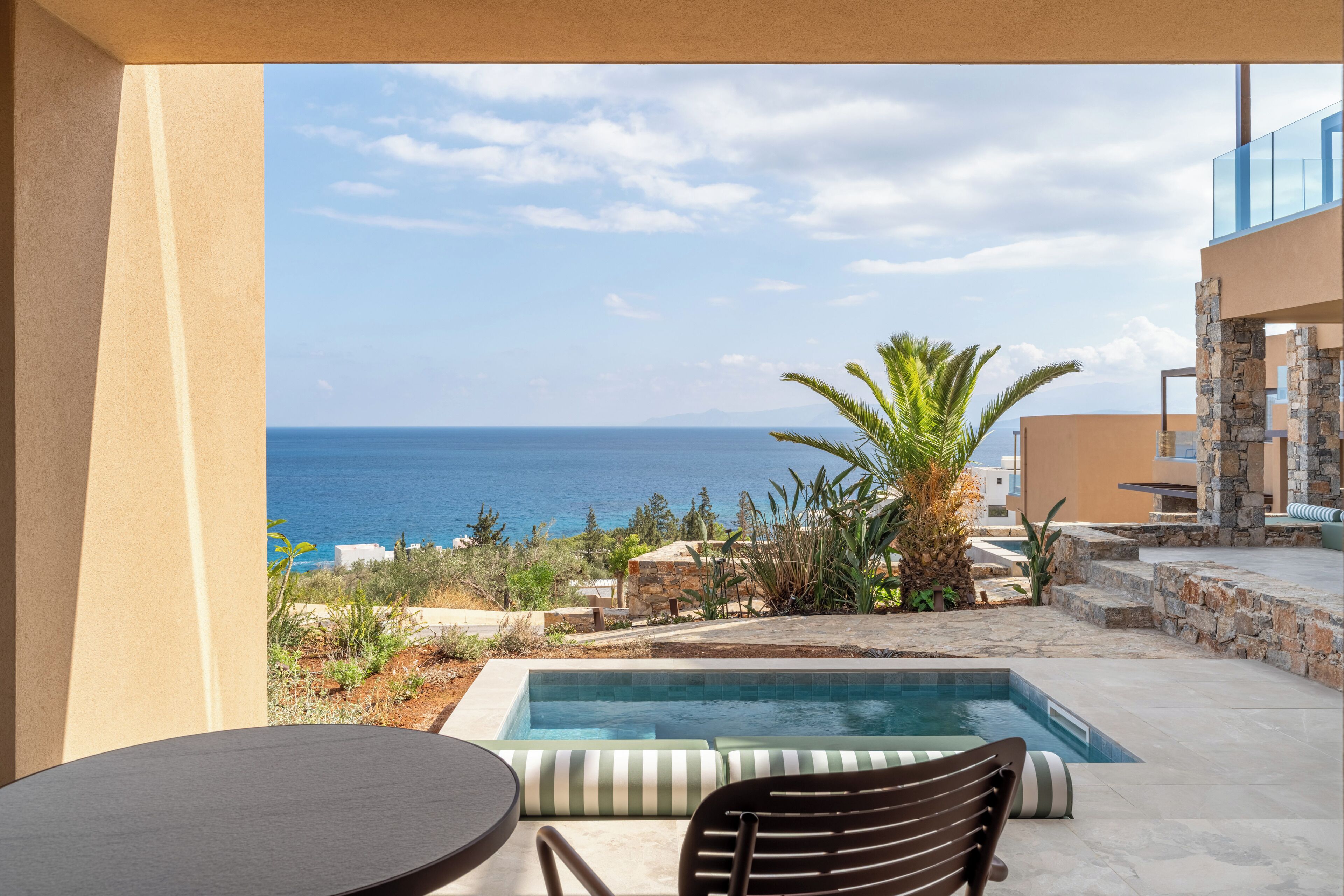 A poolside area with a view of the sea, a table, and a chair.