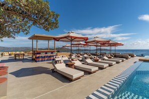 Un área junto a la piscina con tumbonas, sombrillas y un bar.