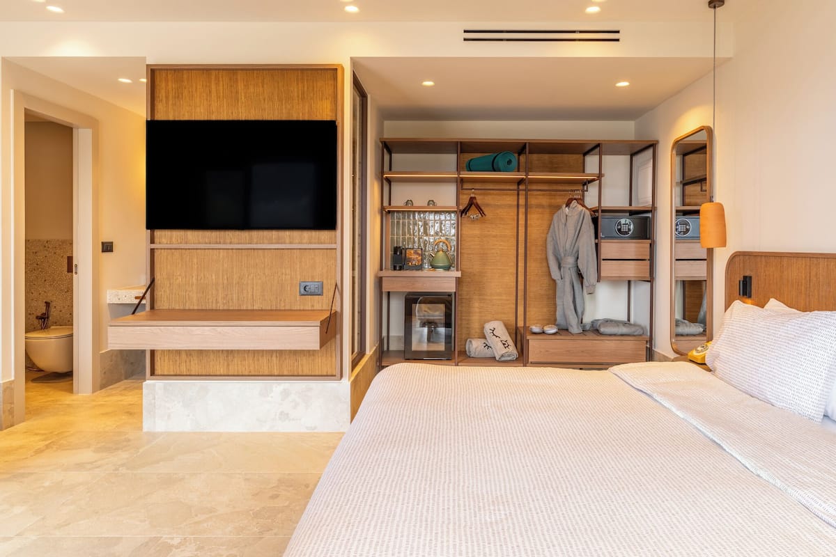 A modern hotel room with a large bed, built-in wardrobe, and a flat-screen TV.