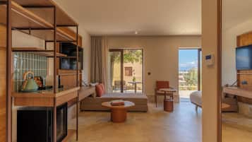 A modern hotel room with a kitchen area, a seating area with a sofa and coffee table, and a balcony with a view.