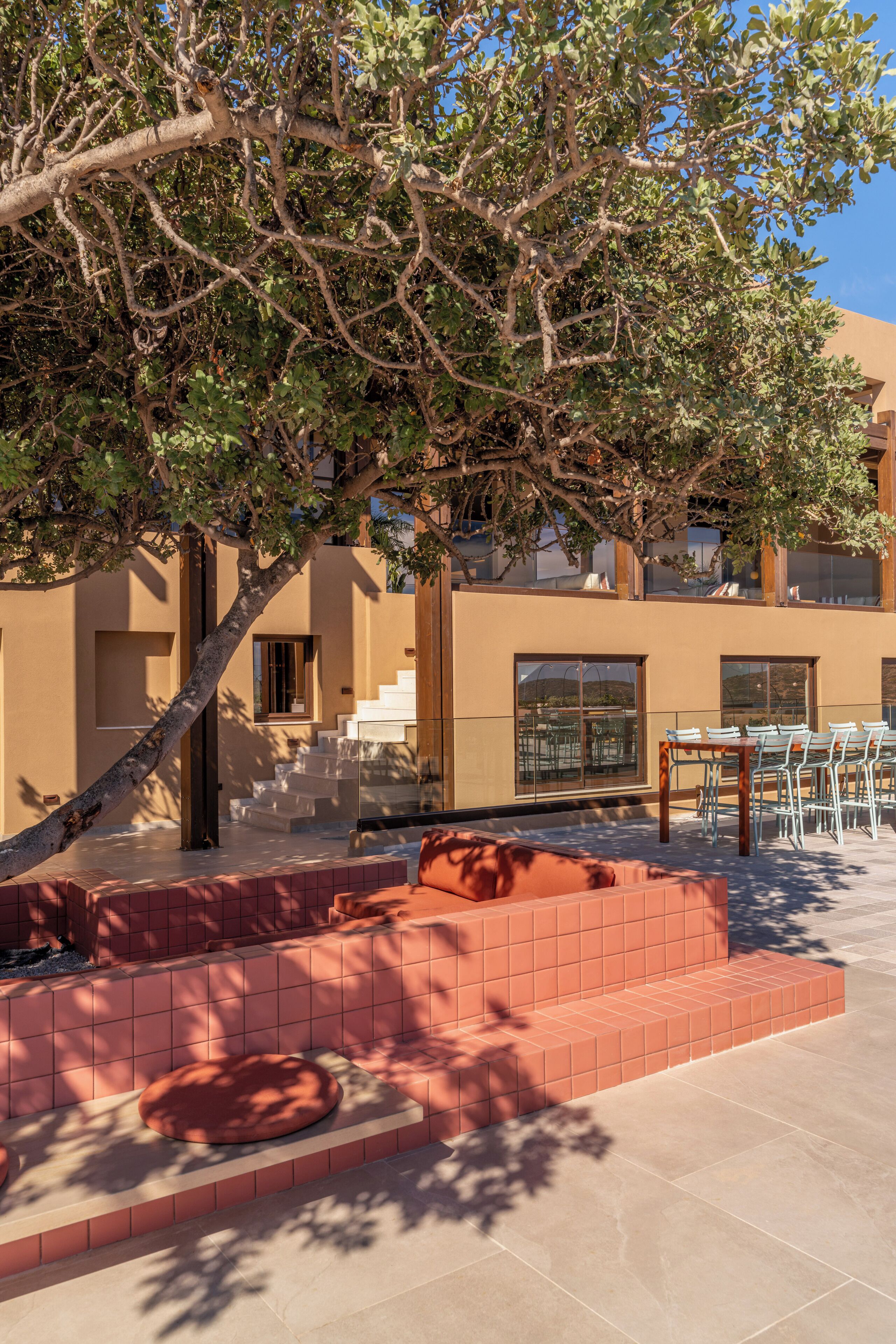A courtyard with a tree, outdoor seating, and a staircase leading to an upper level.