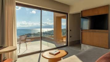 A modern hotel room with a large sliding glass door to a balcony, a flat-screen TV, and a small round table with a book.