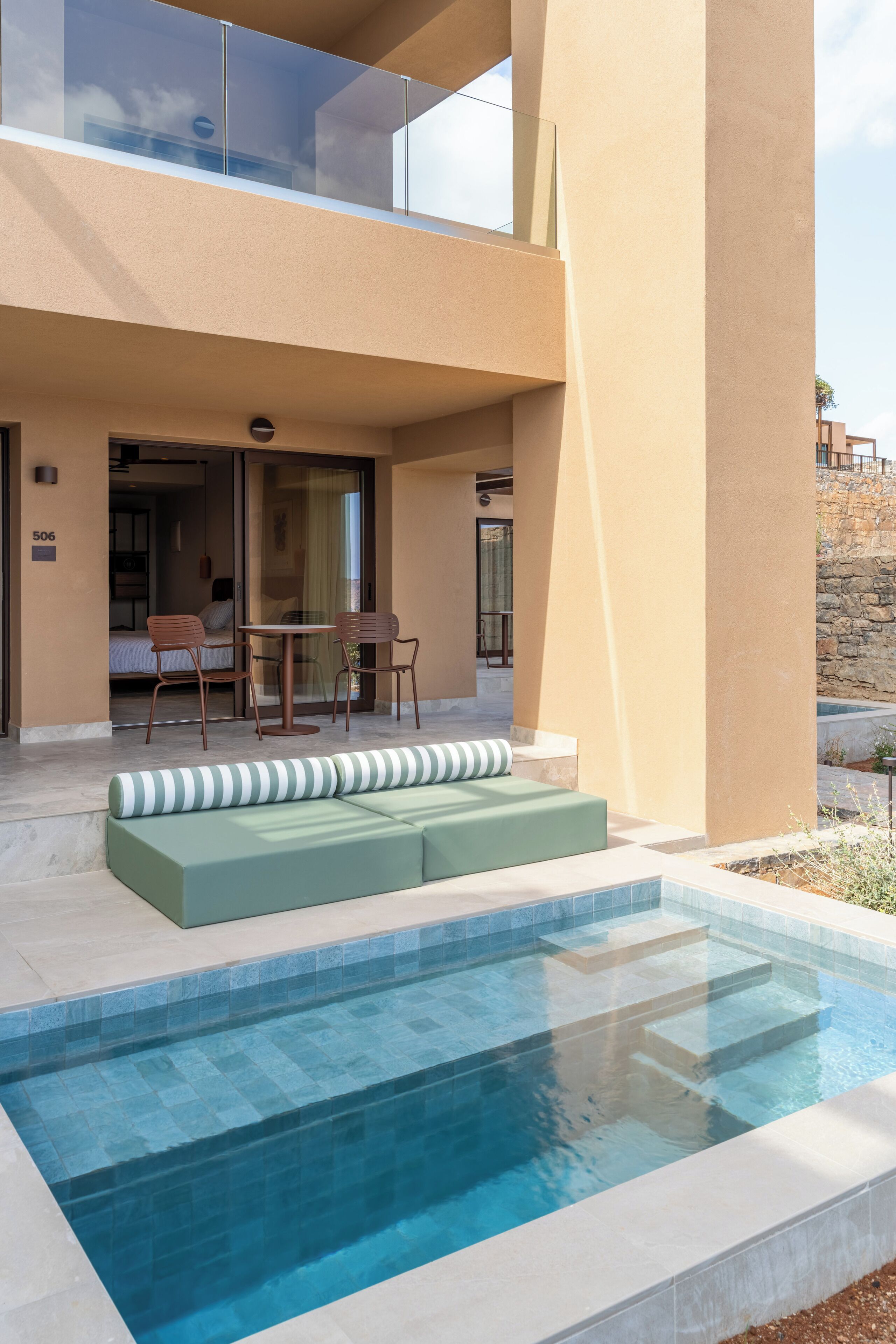 Ein modernes Hotel mit Schwimmbad, Sitzgelegenheiten im Freien und einem gläsernen Balkon.