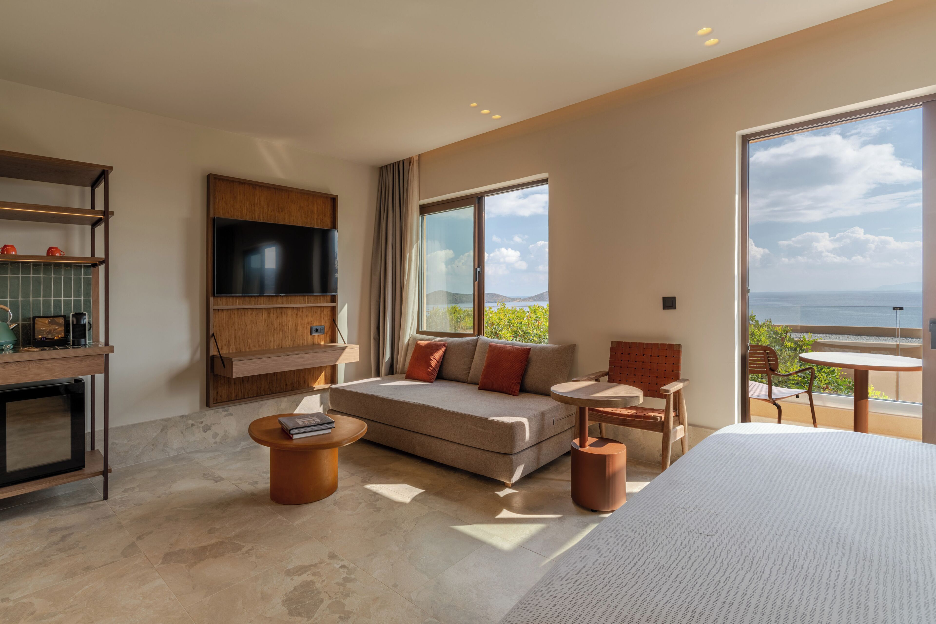 A modern hotel room with a sofa, a small table, a TV, and a balcony with a view.