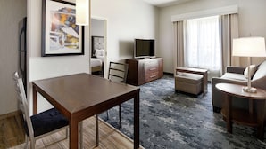 Habitación de hotel con una mesa de comedor de madera, un televisor, un sofá, una silla y una lámpara.