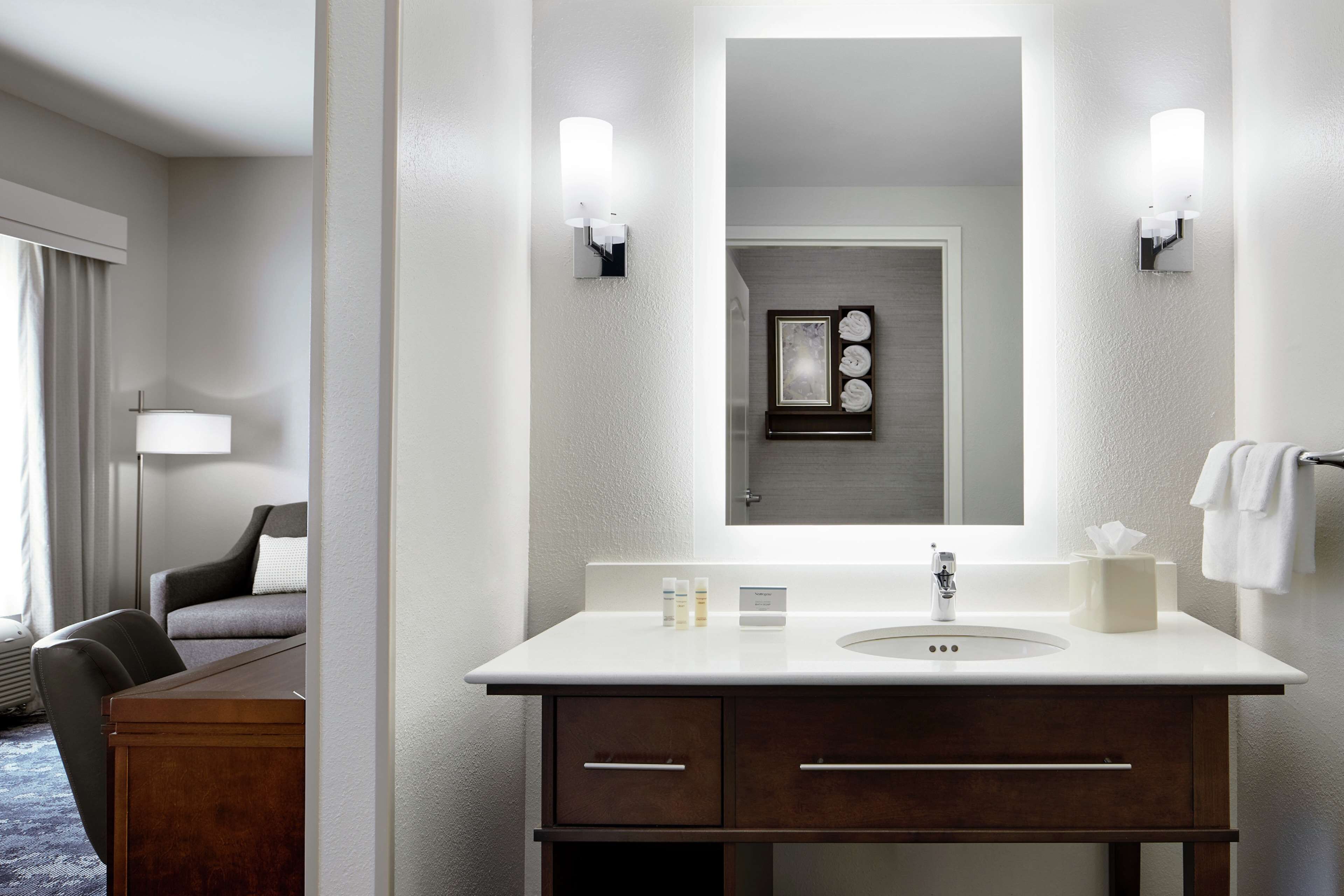 Une salle de bain moderne avec un grand miroir, deux appliques murales, un lavabo et un porte-serviettes.