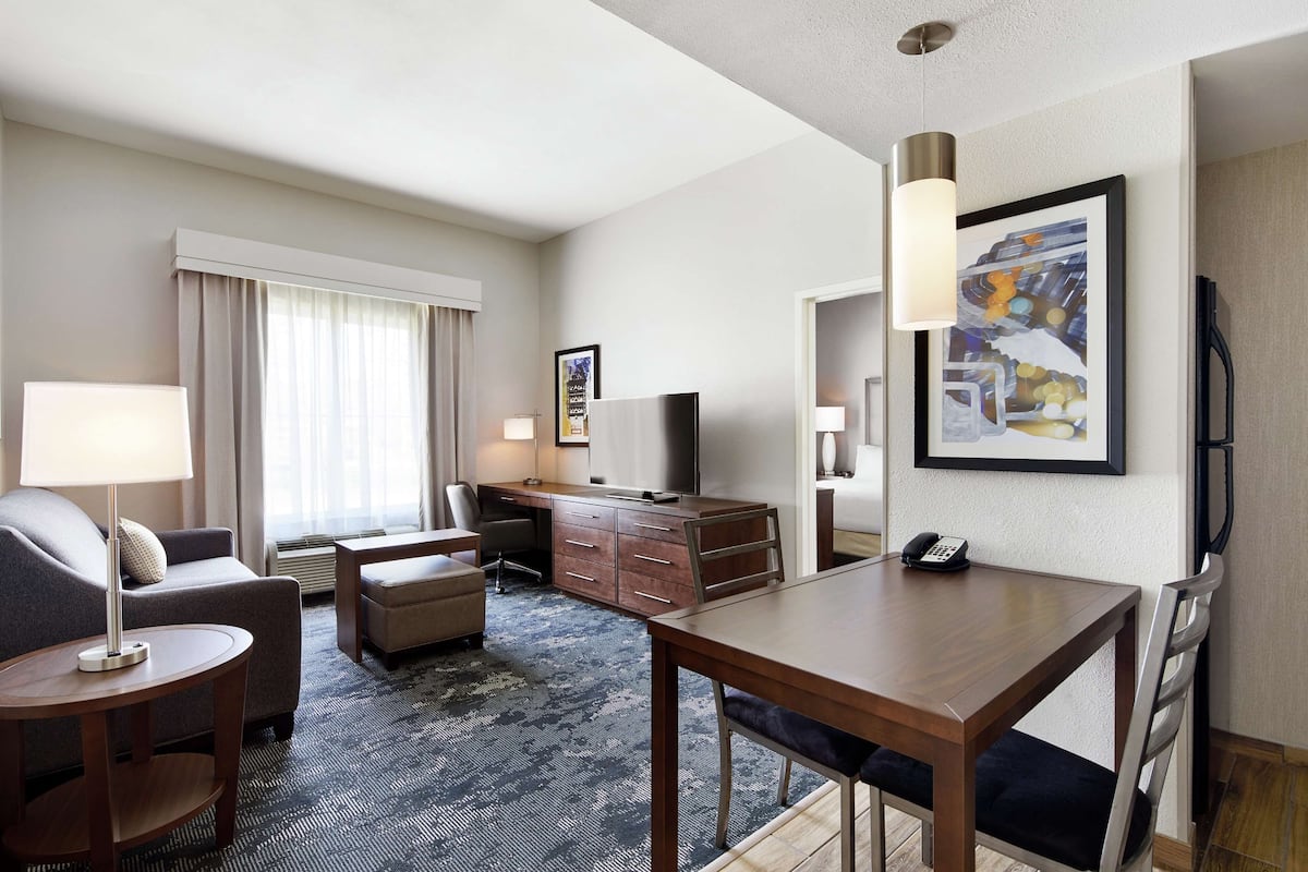 A hotel room with a sofa, a desk, a dining table, and a TV.