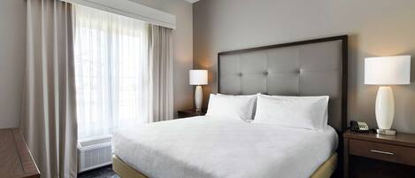 A hotel room with a large bed, a ceiling fan, a nightstand with a lamp, and a window with curtains.
