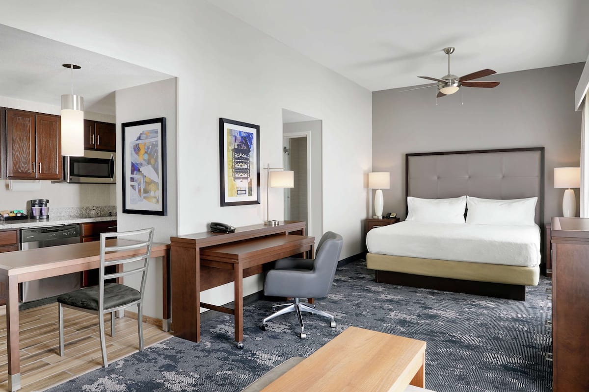 A hotel room with a bed, desk, chair, and kitchenette.