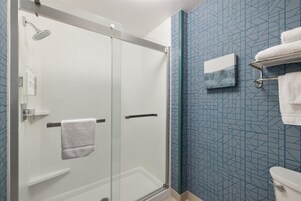 A bathroom with a glass shower enclosure, a white toilet, and a towel rack with towels.