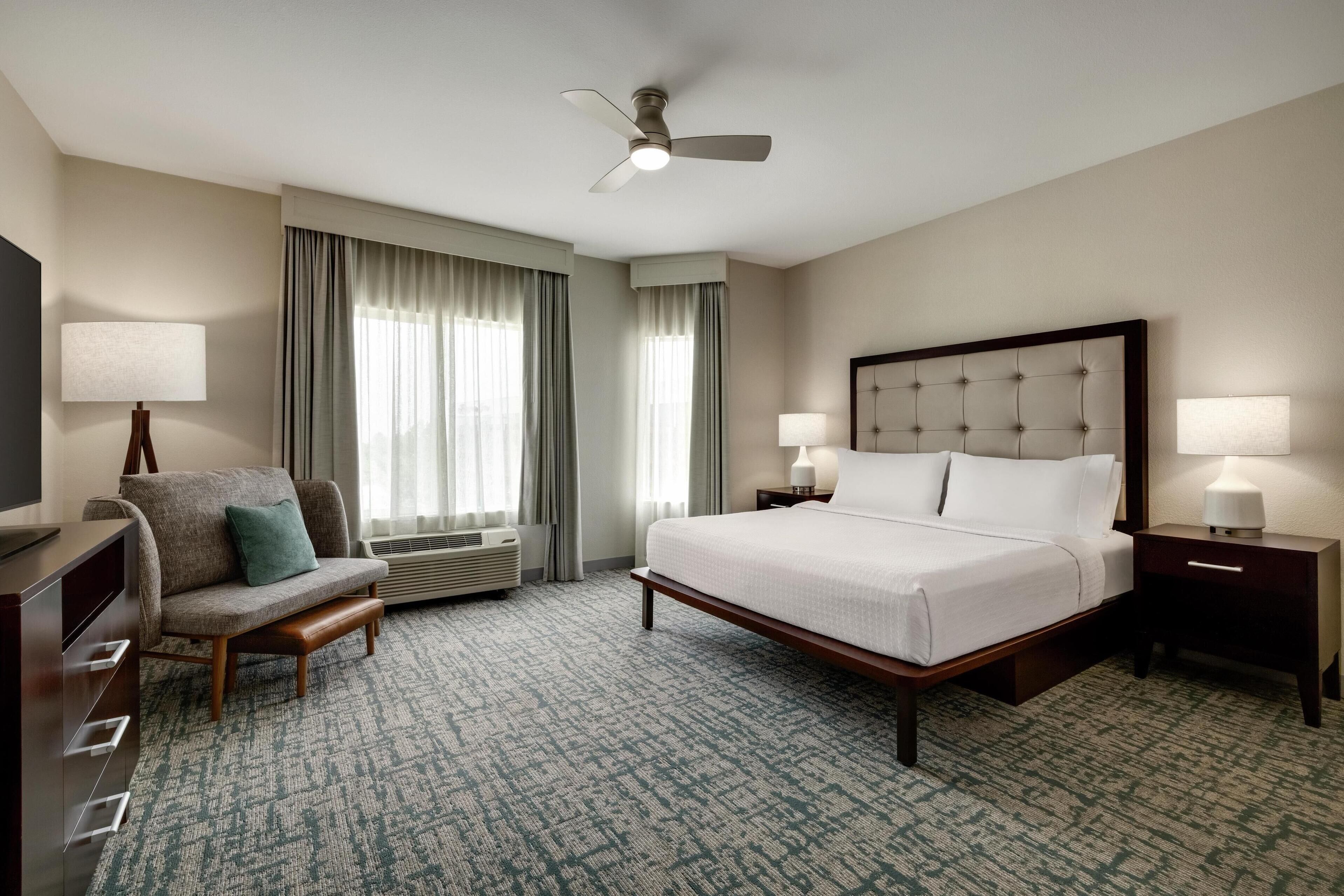 A hotel room with a bed, a chair, a desk, a television, and a ceiling fan.