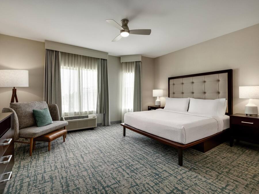 A hotel room with a bed, a chair, a desk, a television, and a ceiling fan.