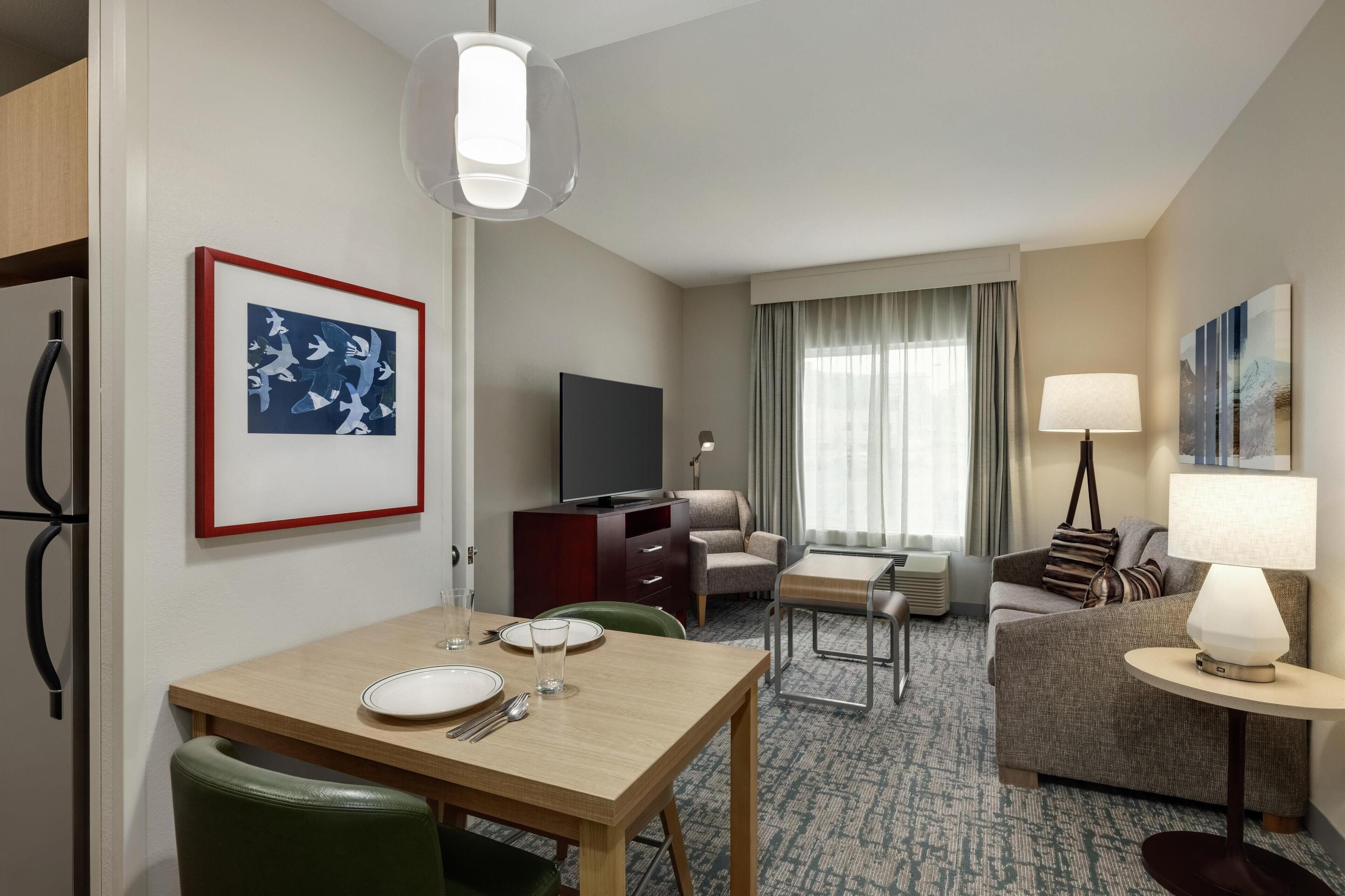 Una camera d'albergo con un tavolo da pranzo, un divano, una TV e una lampada.