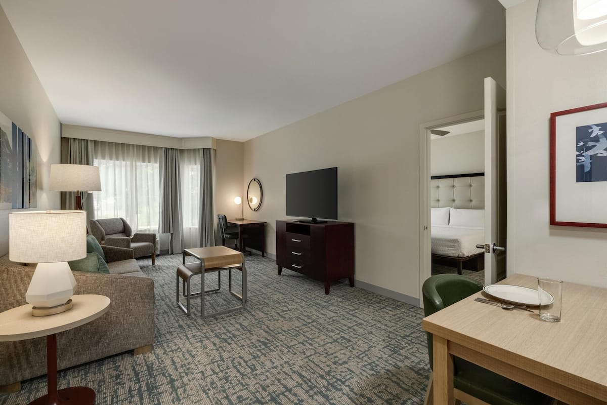 A hotel room with a sofa, a small dining table, a TV, a desk, and a bed.