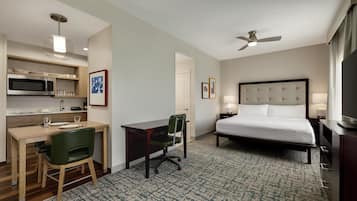 A hotel room with a bed, desk, chair, microwave, and ceiling fan.